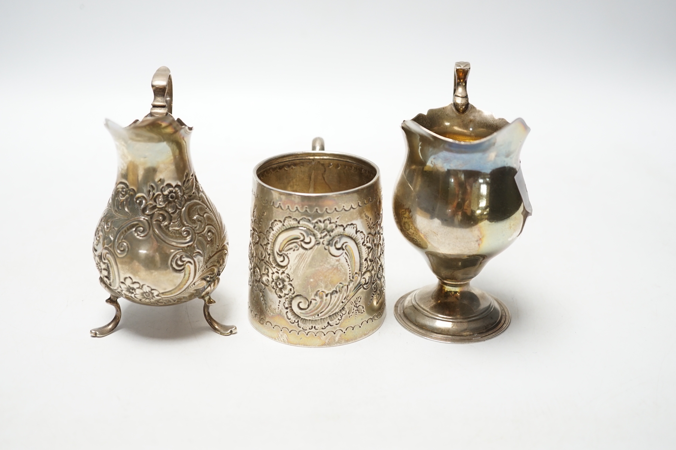 A Victorian silver inverted pyriform cream jug, London, 1886, 10.4cm, another, embossed, Chester, 1896 and an Edwardian silver embossed christening mug, Chester, 1902, 8.1oz.
